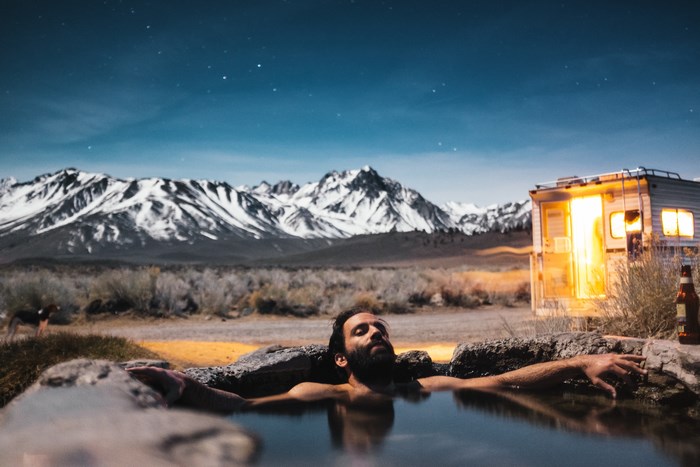 Man relaxing in hot spring near mountains and RV at night