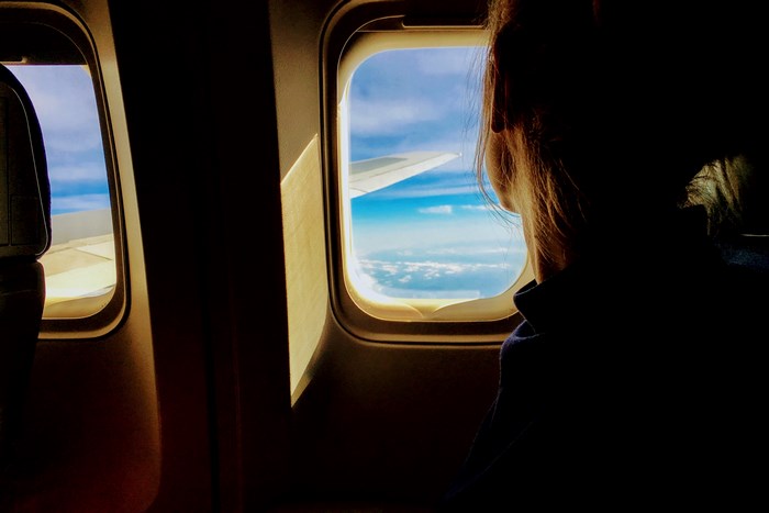 Girl looking out airplane window at clouds and wing