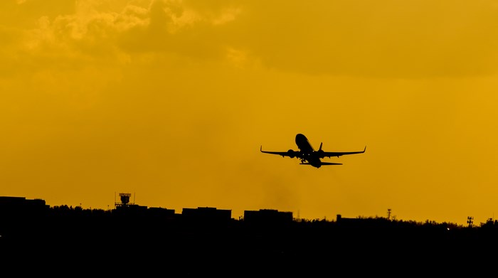 Airplane taking off over city silhouette at sunset