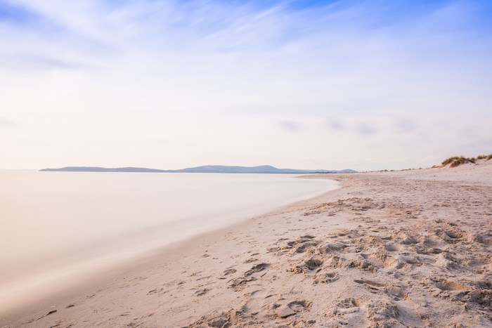 Long exposure beach with distant mountains and blue sky