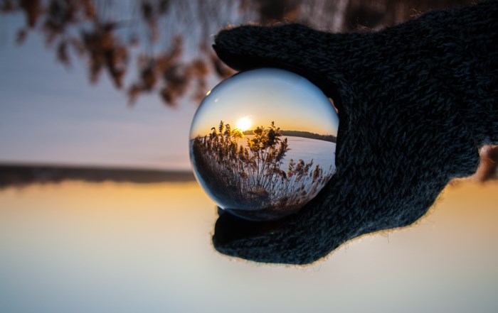 Gloved hand holding a glass ball reflecting a winter sunrise