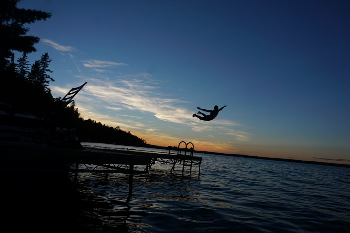 Silhouette of a person diving off a dock at sunset