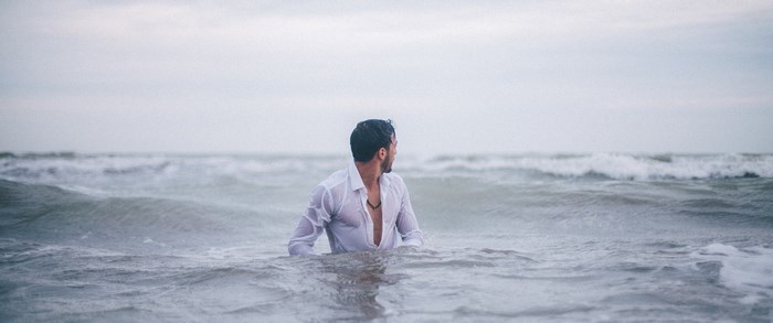 Man in wet white shirt swimming in the ocean waves