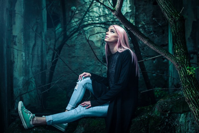 Woman with pink hair sitting in a dark forest
