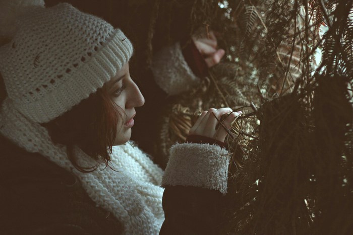 Woman in white knit hat and scarf peeking through branches