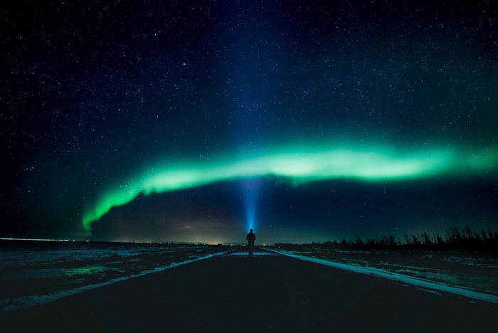 Man with flashlight under Aurora Borealis