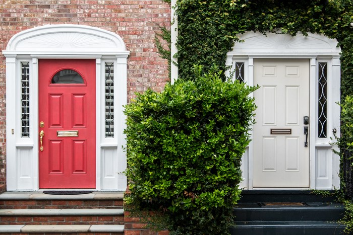 Two doors, red and white, with brick and greenery