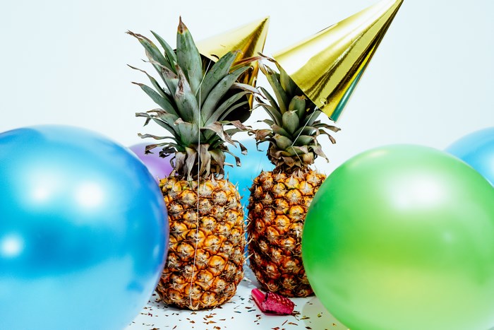 Two pineapples wearing party hats with balloons