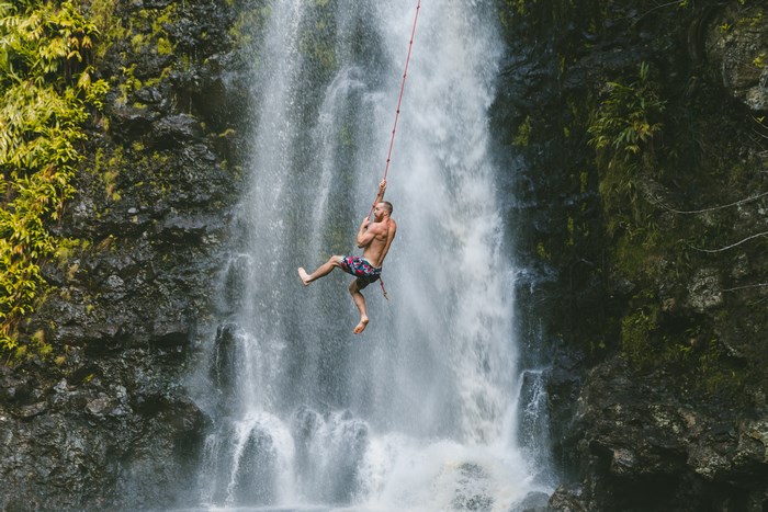 Man swinging on a rope swing in front of a waterfall