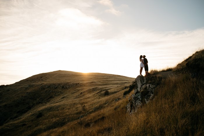 Couple kissing on a grassy hill at sunset in New Zealand
