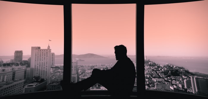 Silhouette of a man sitting by a window overlooking a city