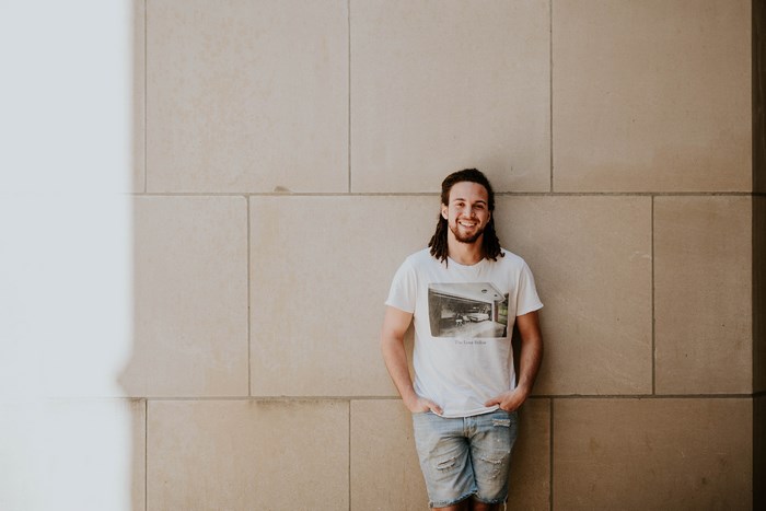 Man with dreadlocks smiling against a stone wall