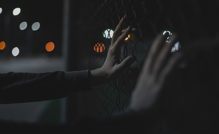 Person touching a chainlink fence at night with bokeh lights