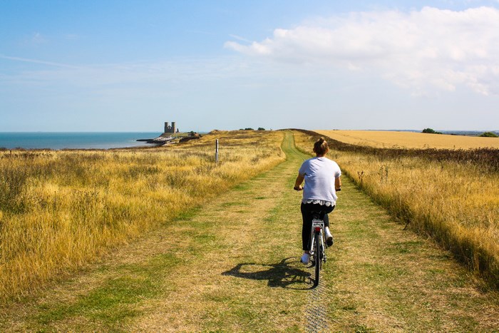 Woman cycling on a path towards castle ruins by the sea