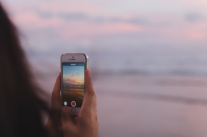 Person holding iPhone recording a sunset at the beach
