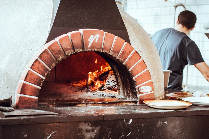 Man cooking in a brick wood-fired pizza oven