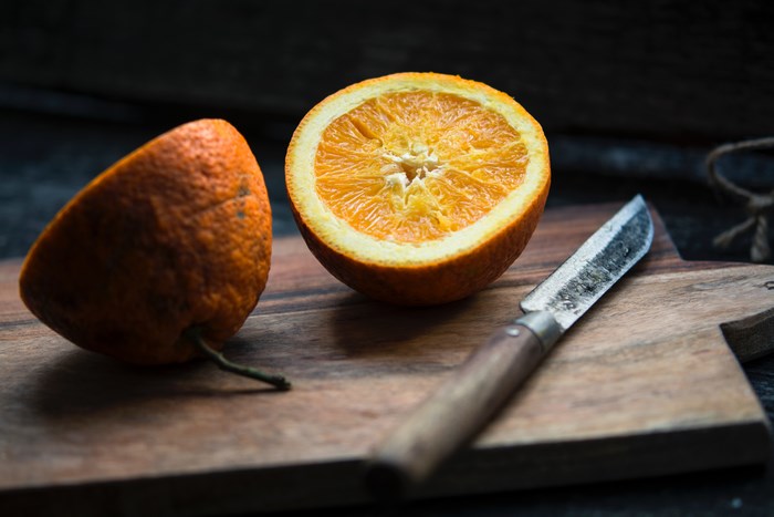 Orange cut in half with a knife on a cutting board