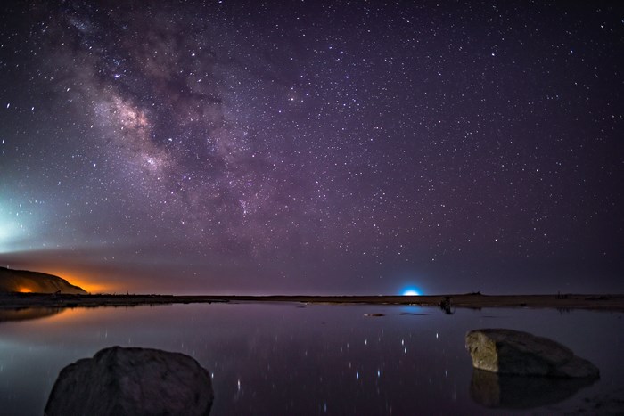 Milky Way over a reflective body of water with rocks