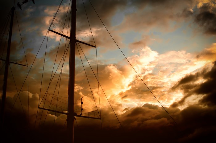 Sailboat masts against a dramatic sunset sky