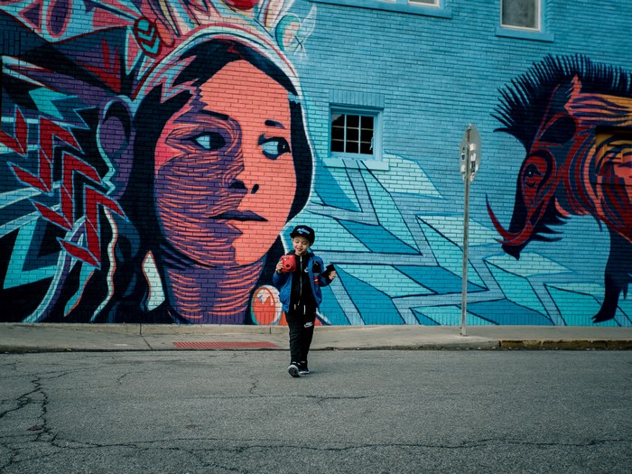 Boy with ball in front of mural with woman and warthog