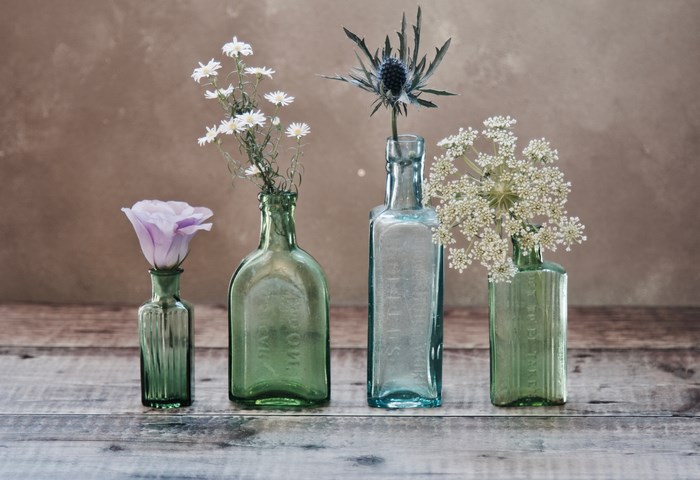 Four glass bottles with flowers on a wooden table