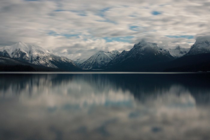 Snow-capped mountains reflected in a calm lake under a cloudy sky