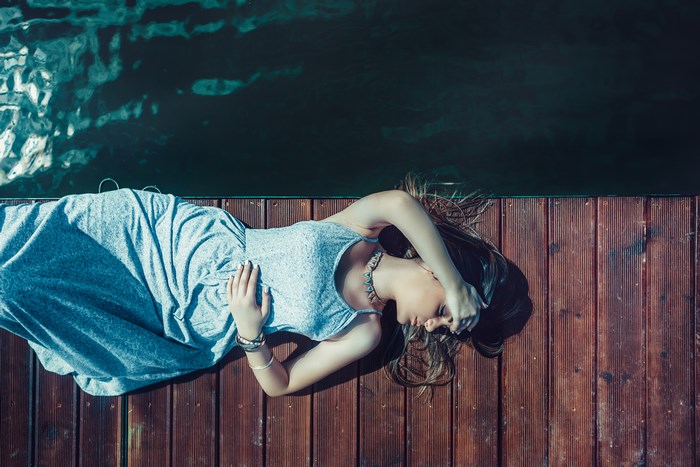 Woman in blue dress lying on a wooden jetty by the water