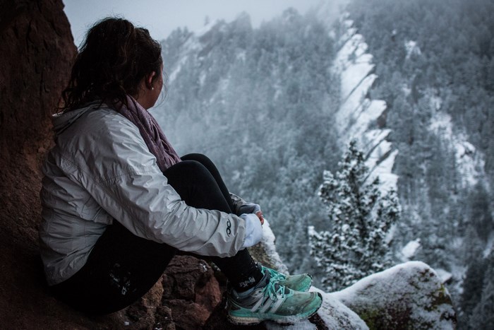Woman Sitting on Rocky Ledge in Snowy Mountain Forest