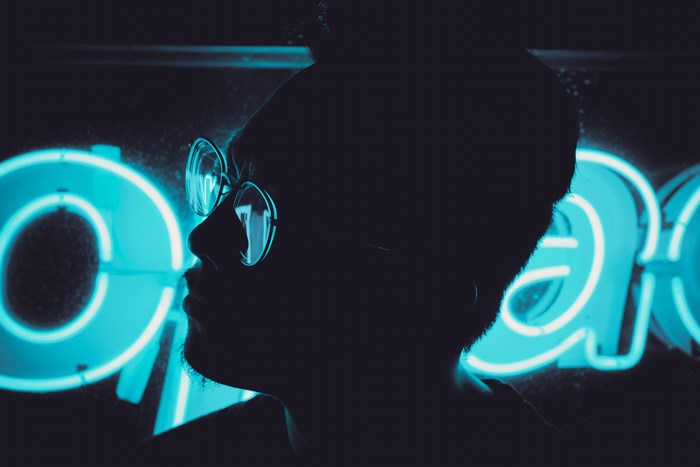 Man in glasses silhouetted against blue neon sign