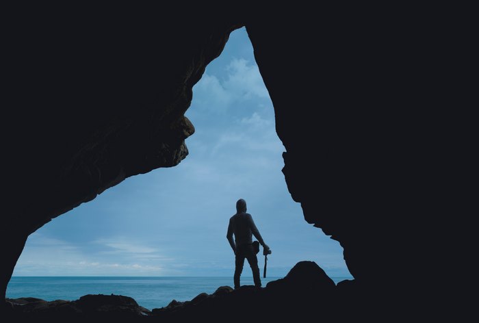 Silhouette of a man with a camera in a cave overlooking the ocean