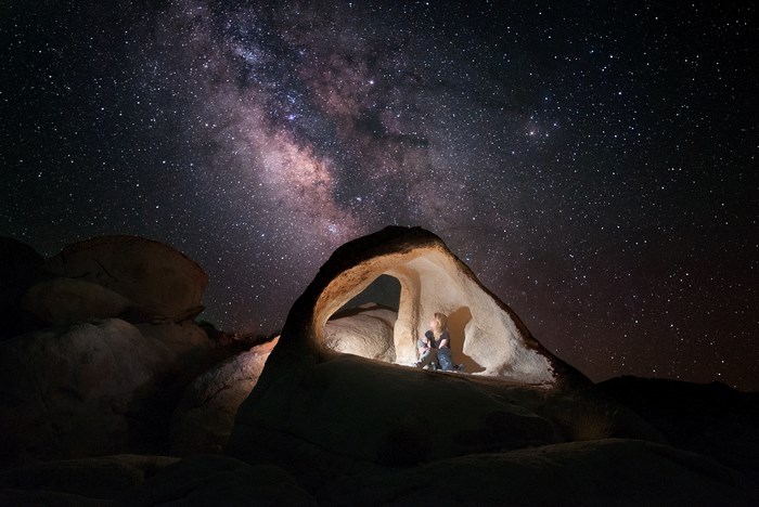 Person sitting in a rock formation under the Milky Way