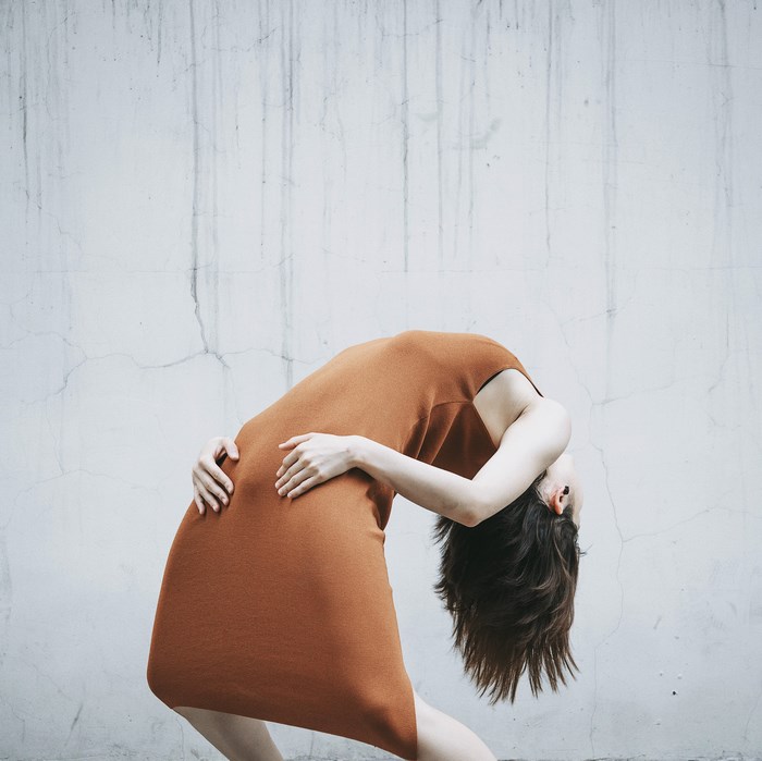 Woman in orange dress bending against a wall