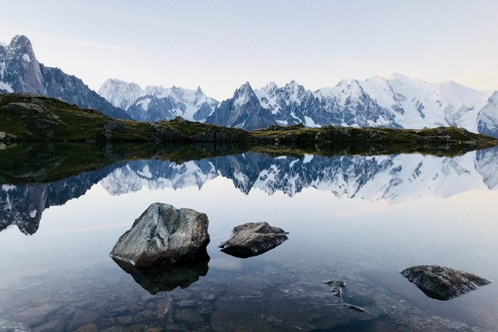 Snow-capped mountains reflected in a calm lake with rocks