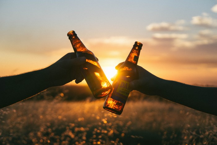 Two hands holding beer bottles at sunset