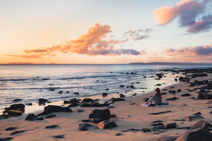 Woman sitting on a beach at sunset