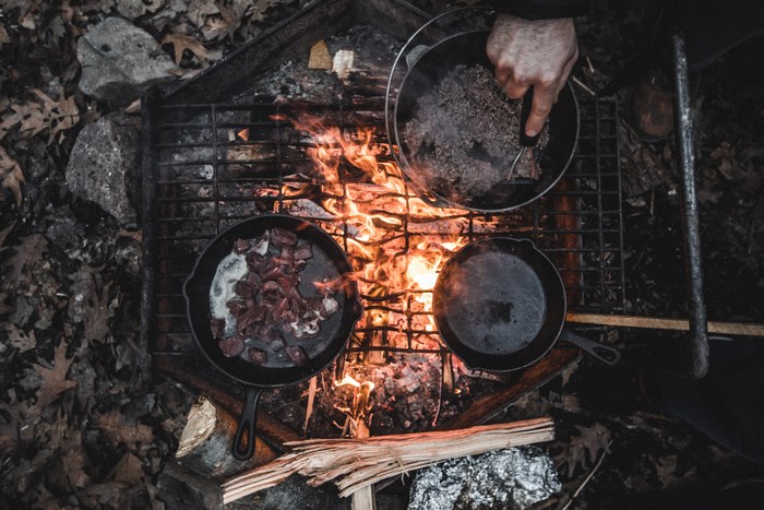 Cooking meat in cast iron pans over a campfire