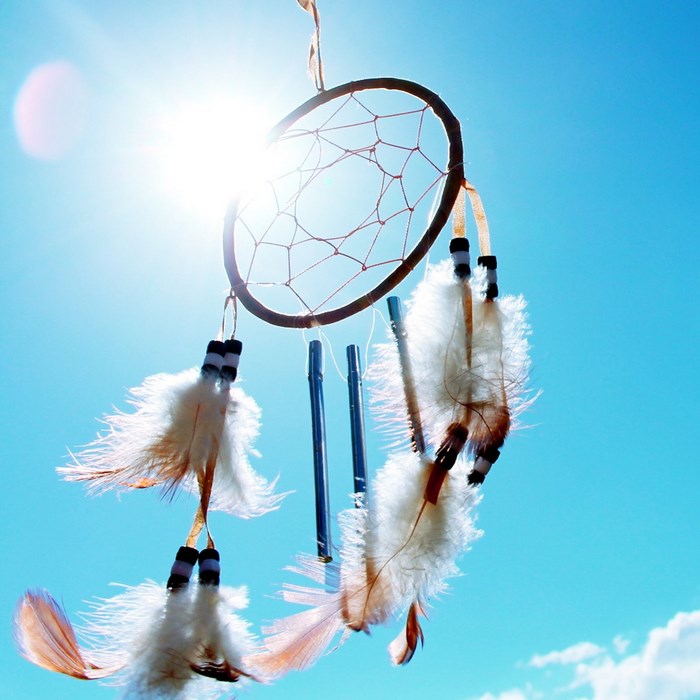 Dream catcher with feathers against blue sky and sun