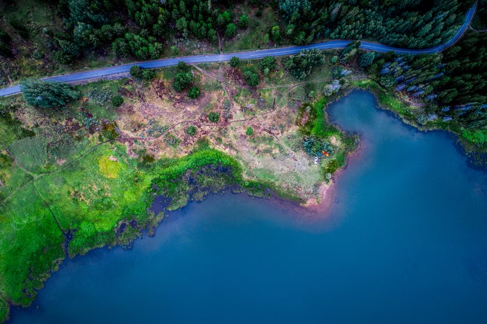 Aerial view of a winding road along a forest and a blue lake