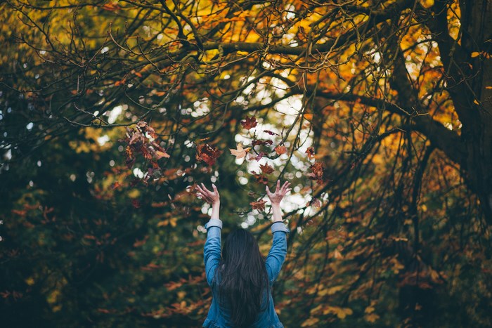 Woman throwing leaves in autumn park
