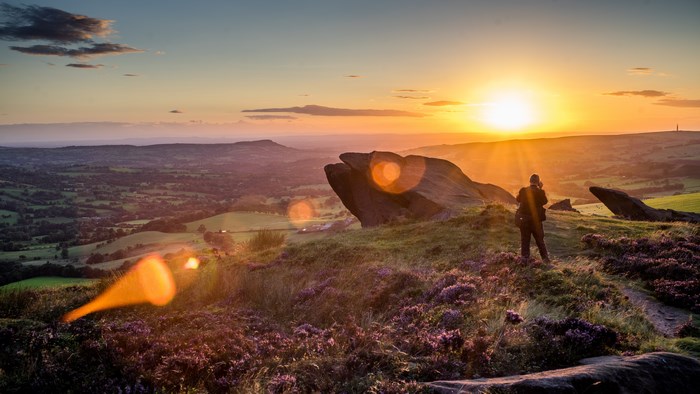 Person photographing sunset over heather valley with rock formations