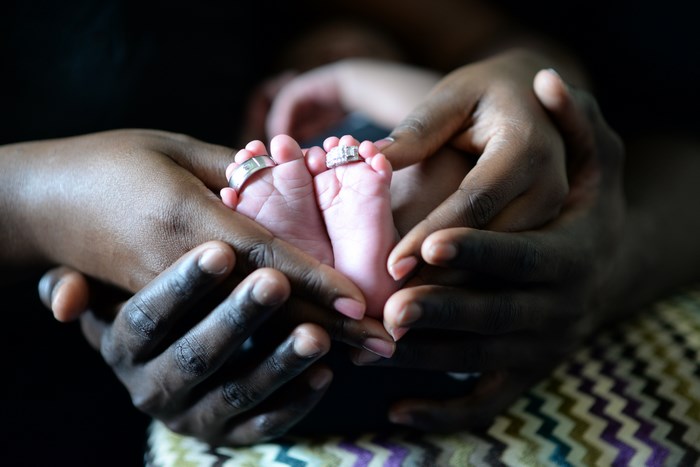 Couple holding newborn baby feet with wedding rings