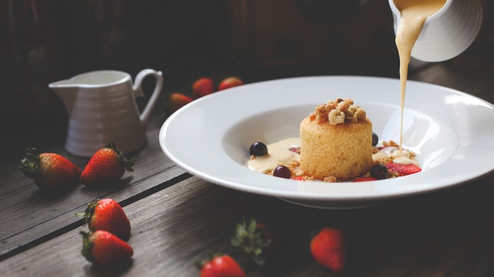 Dessert with custard and strawberries being poured