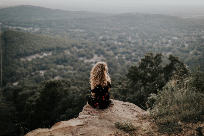 Woman sitting on a cliff overlooking a forest