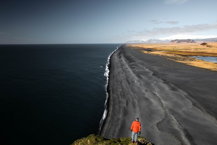 Man standing on cliff overlooking black sand beach in Iceland