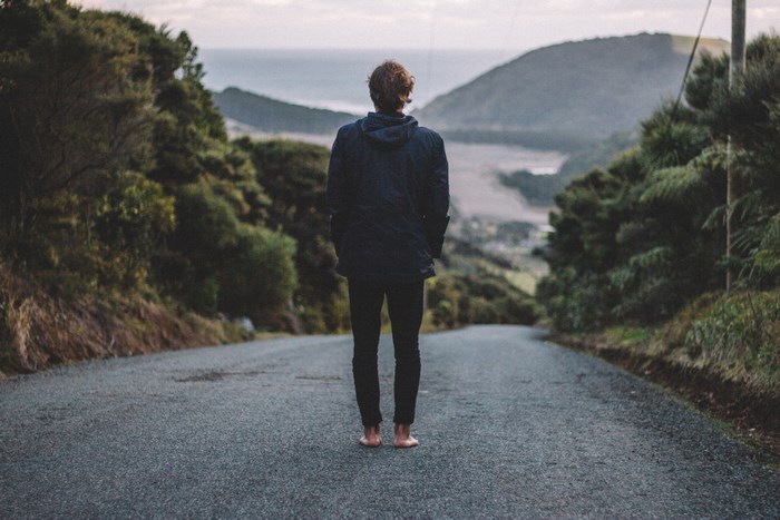 Man standing barefoot on a road overlooking a bay