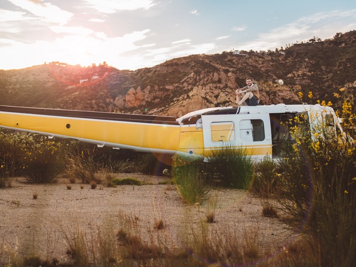 Man sitting on abandoned helicopter at sunset