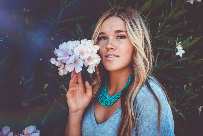 Woman with blonde hair holding pink flowers and wearing a necklace