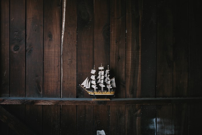 Model sailboat on a wooden shelf against a wooden wall