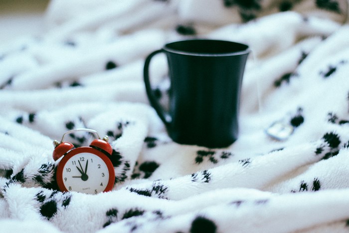 Red alarm clock and black mug on a blanket