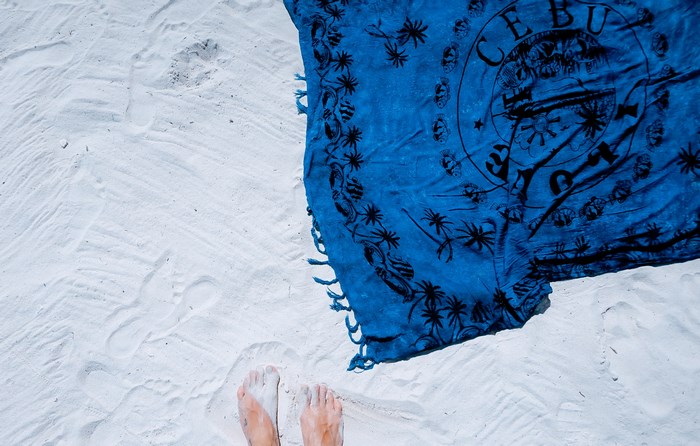 Blue Cebu towel on white sand with feet